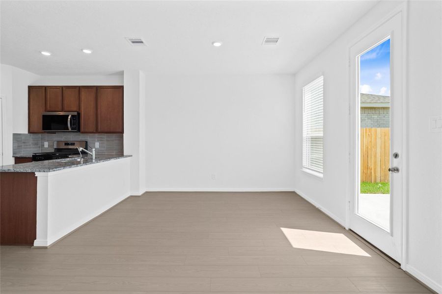 Start your day with a warm cup of coffee and quality time in this charming dining area! Highlights include a large window with blinds, custom neutral paint, vinyl plank flooring, recessed lighting, high ceilings, and a convenient door leading to the rear patio slab and backyard.