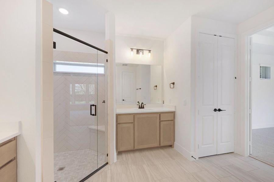 Bathroom with glass walk-in shower, herringbone tile, wood vanity, and double closet doors