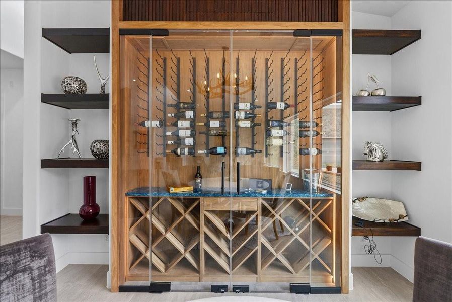 The elegant dining area features a custom climate controlled wine display with integrated lighting, wood accents, and floating shelving.