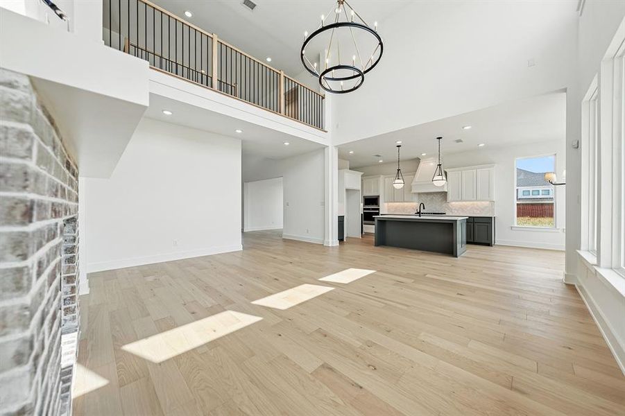 Unfurnished living room featuring a chandelier, recessed lighting, light wood-style floors, a fireplace, and a high ceiling