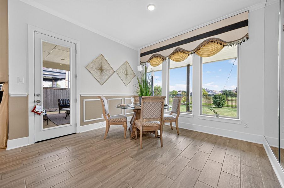 This bright dining area features large windows with elegant drapery, offering a scenic view of the backyard. The space includes a small dining set on wood-style flooring, and a door leading to a cozy outdoor patio. This bright dining area features large windows with elegant drapery, offering a scenic view of the backyard. The space includes a small dining set on wood-style flooring, and a door leading to a cozy outdoor patio.