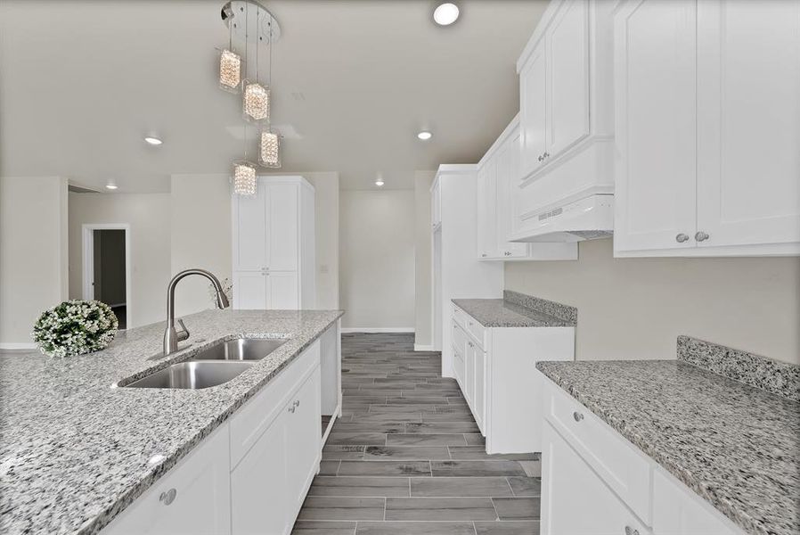 Kitchen featuring under cabinet range hood, recessed lighting, light stone countertops, and white cabinetry