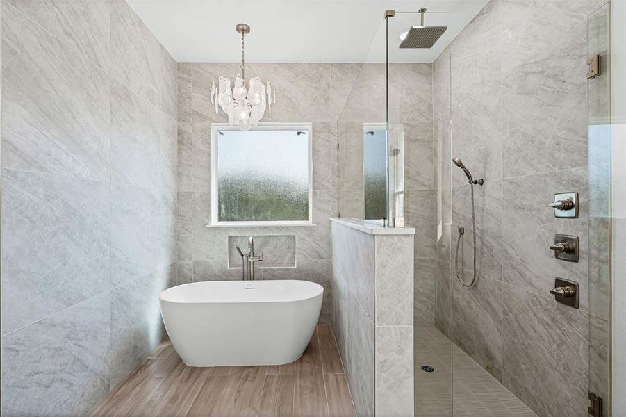 Bathroom featuring tile walls, a soaking tub, walk in shower, a chandelier, and wood finished floors Bathroom featuring tile walls, a soaking tub, walk in shower, a chandelier, and wood finished floors
