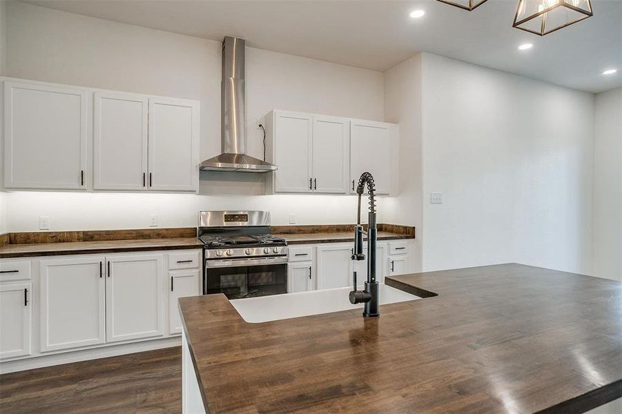 Kitchen featuring butcher block counters, wall chimney exhaust hood, stainless steel range with gas cooktop, and white cabinetry