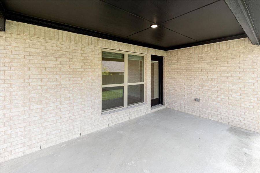 Covered back patio with concrete floor, brick walls, dark ceiling, and sliding glass door entry.