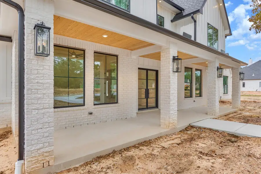 Inviting front porch with stylish black-accented lighting, warm wood soffit detail, and elegant double glass doors creating a polished modern farmhouse entry.