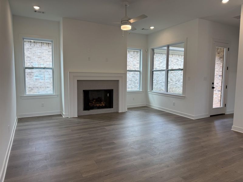 Spacious living area featuring a central fireplace with white mantel, wood-finish flooring, recessed lighting, and a ceiling fan