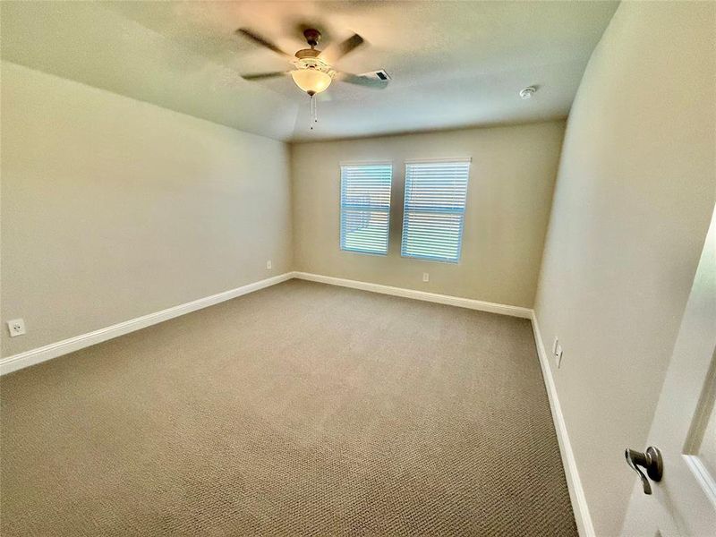 Spacious room featuring neutral carpeting, two windows with blinds, a ceiling fan with integrated lighting, and white baseboards Spacious room featuring neutral carpeting, two windows with blinds, a ceiling fan with integrated lighting, and white baseboards