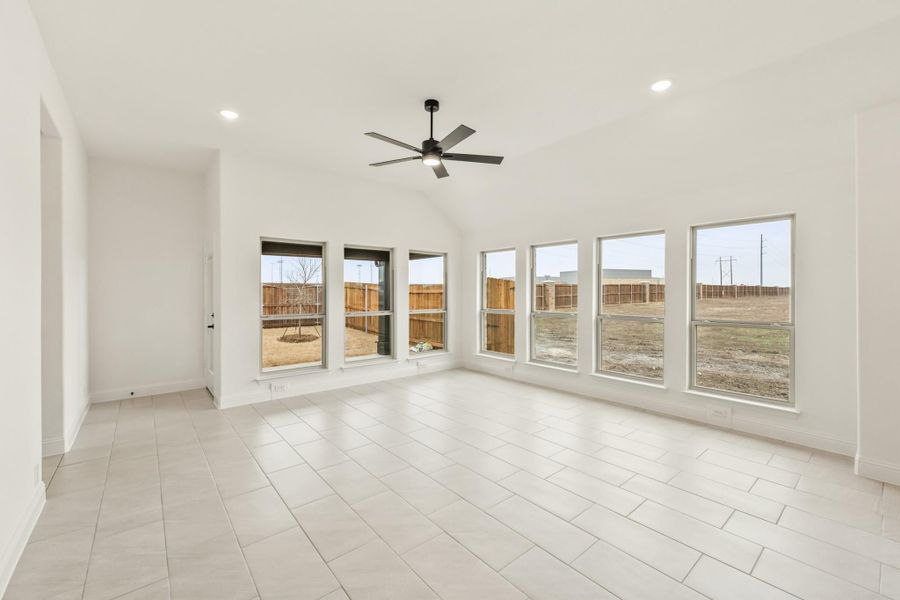 Empty living room with vaulted ceiling, ceiling fan, tile floors, and large windows overlooking fenced backyard