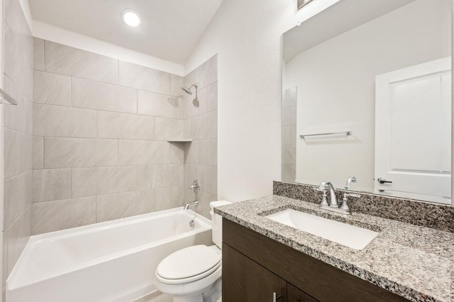 Bathroom with tiled tub-shower combo, granite vanity countertop, dark wood cabinets, and large mirror