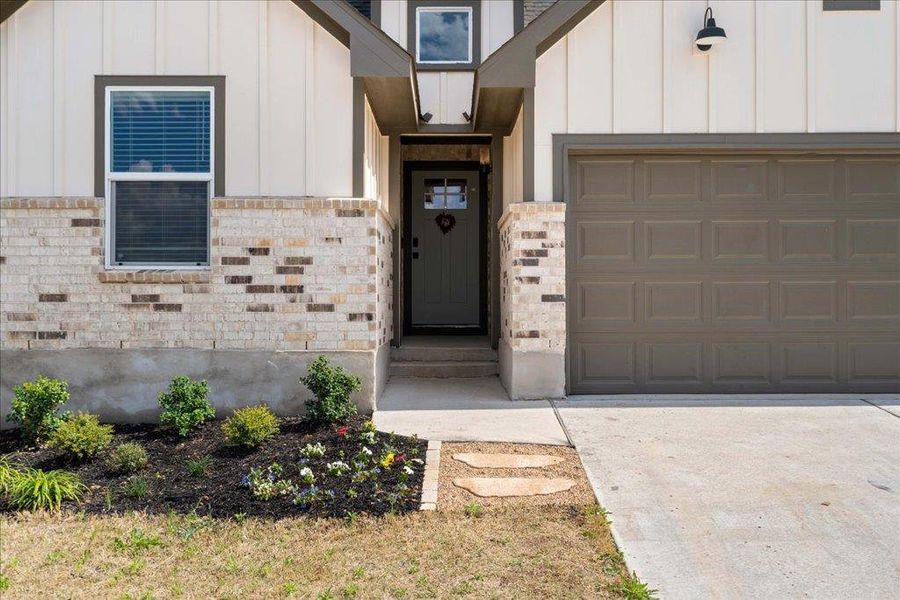Entrance to property with brick siding, a garage, board and batten siding, and concrete driveway