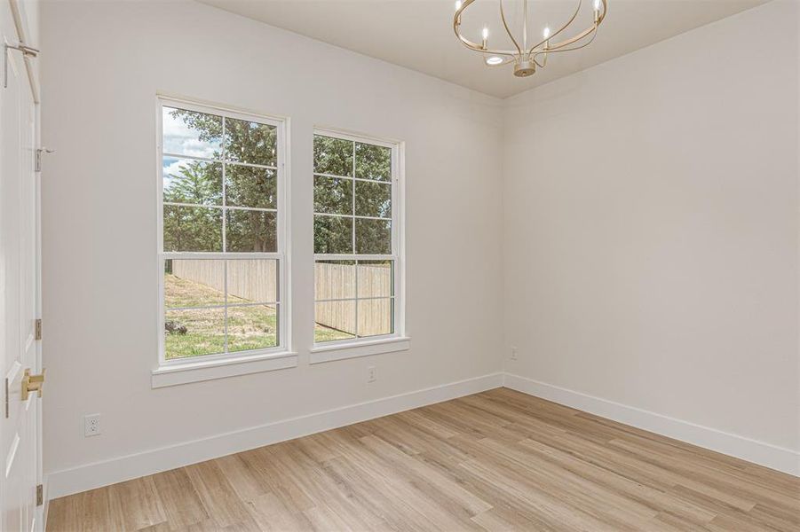 Room featuring two double-hung windows, wood-finish flooring, a contemporary chandelier, white baseboards, and a paneled interior door with brass hardware