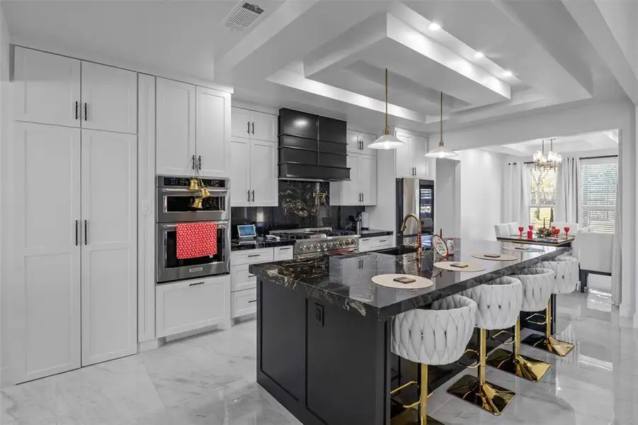 Kitchen featuring a raised ceiling, dark cabinets, a breakfast bar, a large island with sink, and white cabinetry Kitchen featuring a raised ceiling, dark cabinets, a breakfast bar, a large island with sink, and white cabinetry