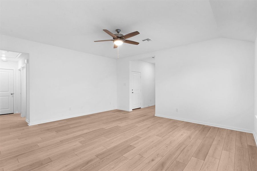 Empty room with attic access, light wood-style flooring, ceiling fan, and lofted ceiling