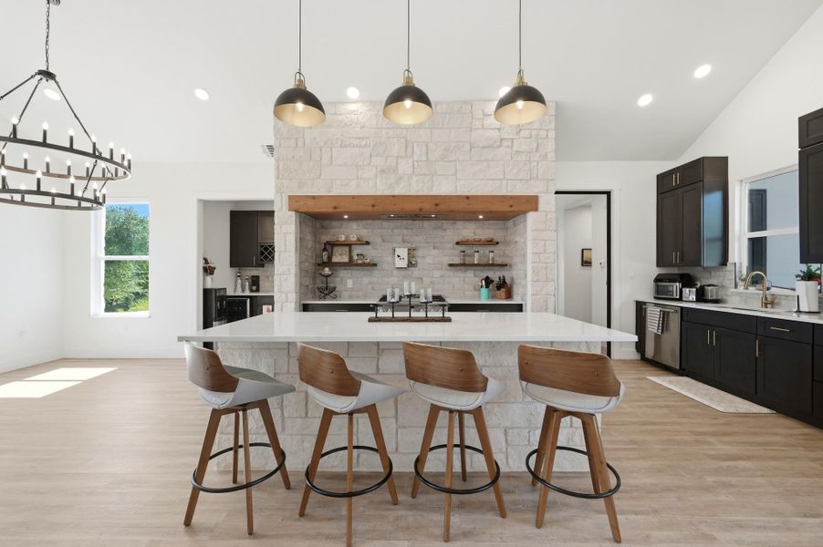 An open kitchen layout features a large stone island and soaring vaulted ceilings.