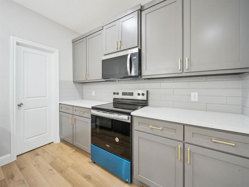 Kitchen featuring gray cabinets, light wood-type flooring, stainless steel appliances, and tasteful backsplash