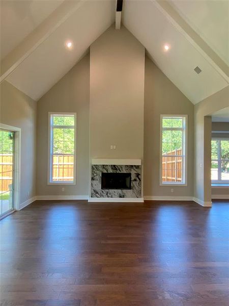 Unfurnished living room featuring beam ceiling, a healthy amount of sunlight, high vaulted ceiling, and a high end fireplace