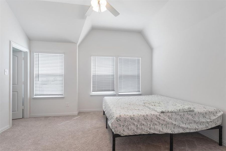 Bedroom featuring light colored carpet, vaulted ceiling, and ceiling fan