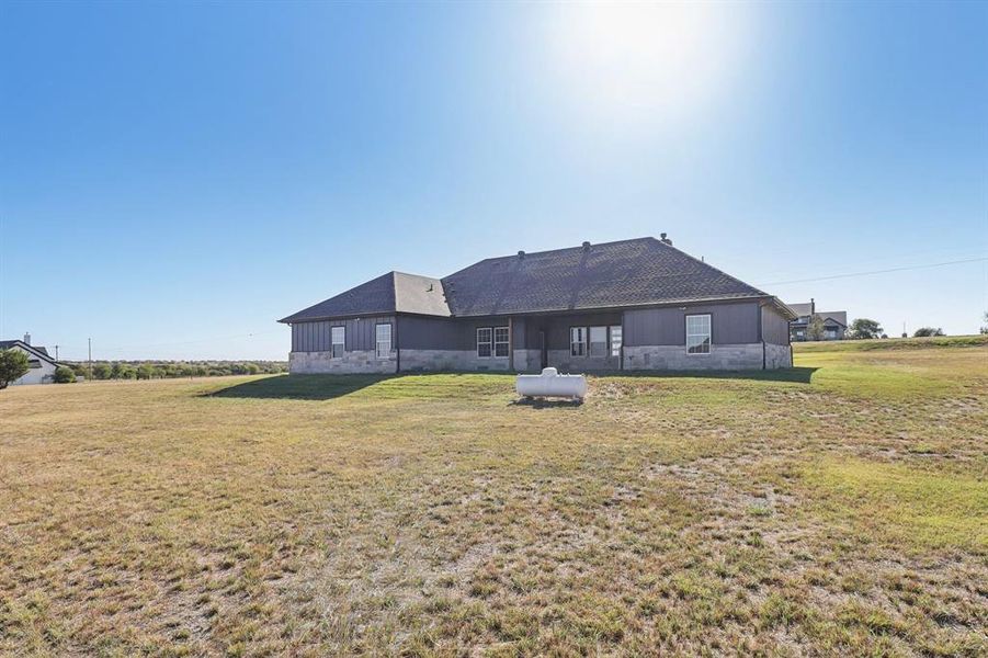 Back of house featuring a lawn, a patio area, and a shingled roof