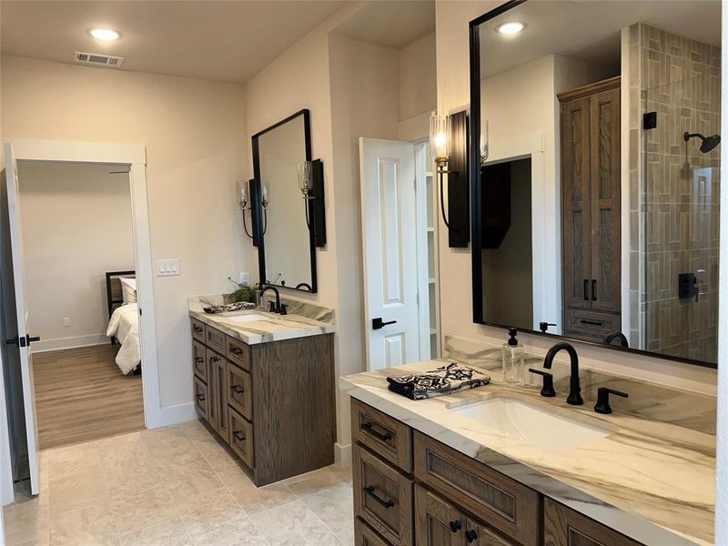 Bathroom featuring dual vanities with wood-finish cabinetry, white countertops with natural veining, and matte black fixtures