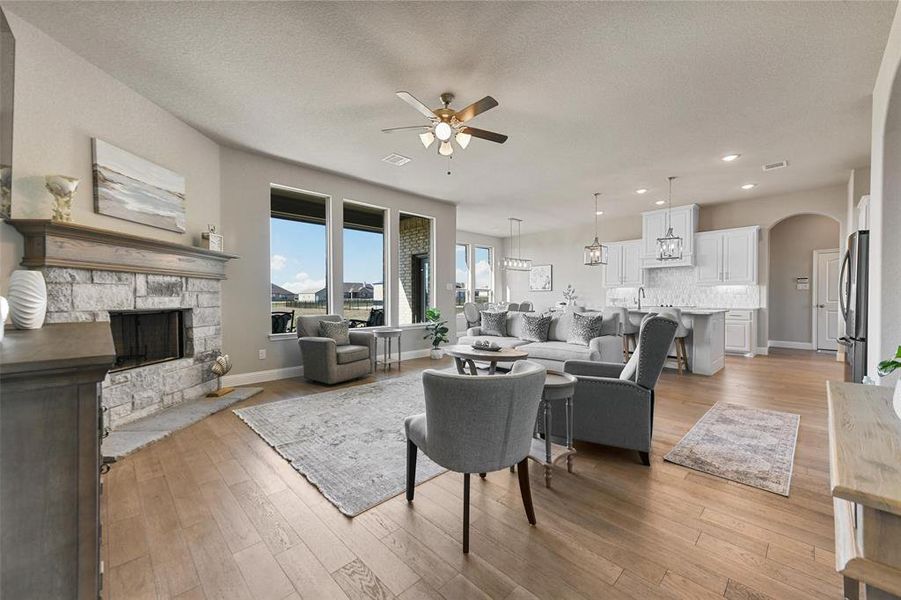 Living room featuring a fireplace, a textured ceiling, light wood-type flooring, and ceiling fan