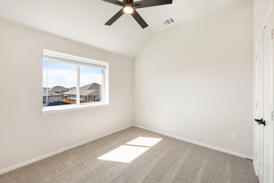 Empty bedroom with vaulted ceiling, ceiling fan, carpet flooring, and a window with neighborhood view.