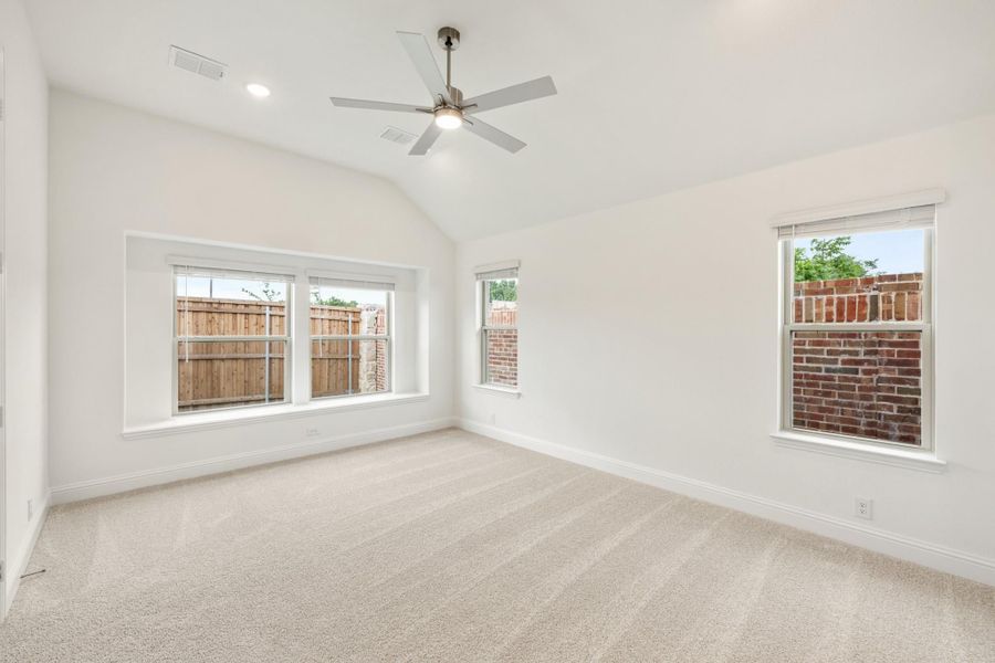 Empty bedroom with vaulted ceiling, ceiling fan, carpet flooring, and multiple windows with natural light