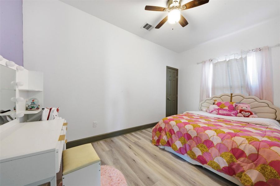 This cozy bedroom features a bright atmosphere with white walls and light wood flooring. It includes a ceiling fan and offers a charming and functional space.