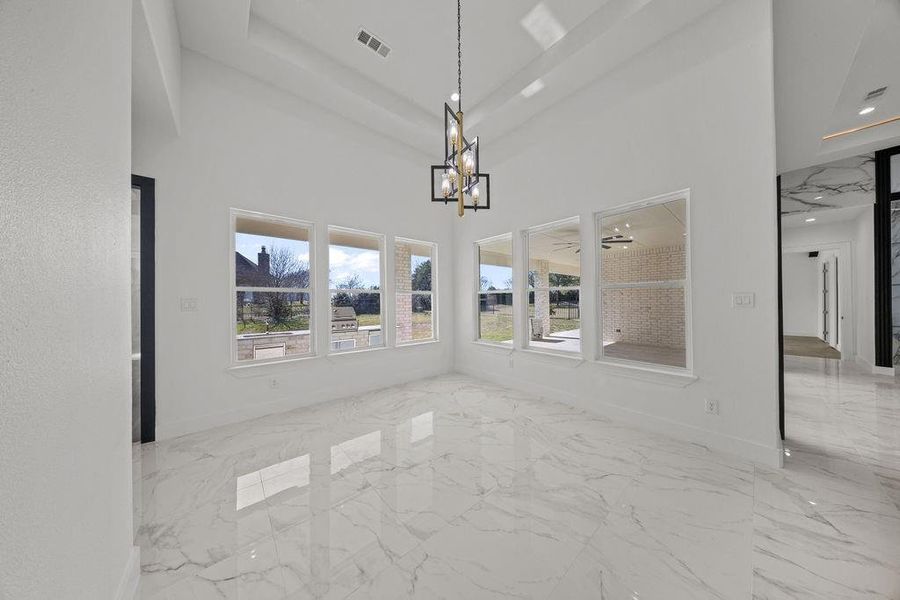 Unfurnished dining area with light marble finish flooring, hanging lights, and a high ceiling