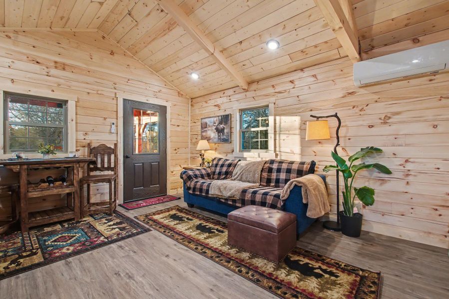 Living area with wood ceiling, wood finished floors, lofted ceiling, wood walls, and an AC wall unit