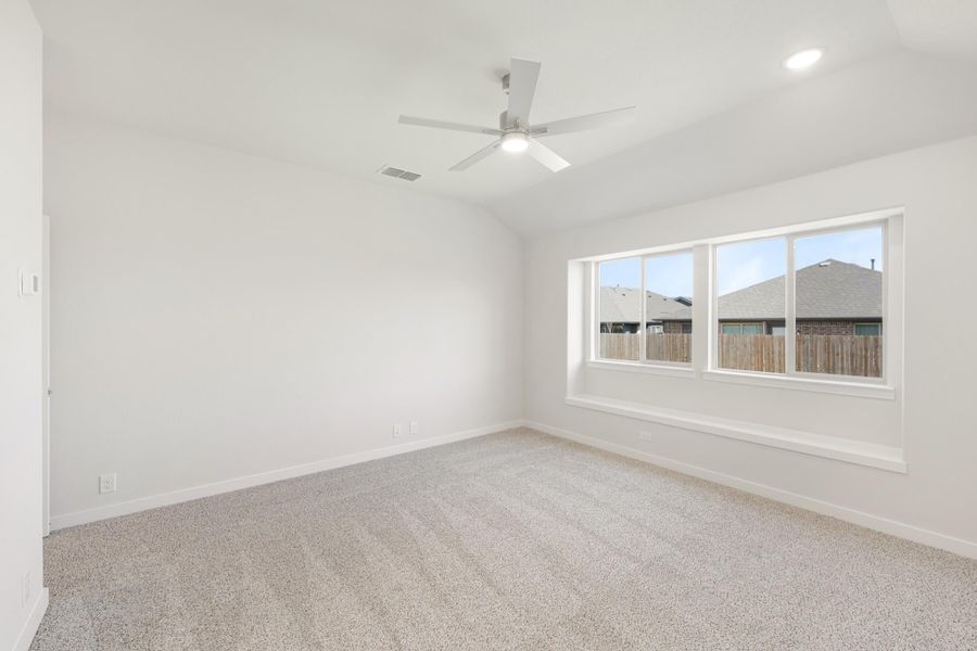 Empty bedroom with vaulted ceiling, ceiling fan, carpet flooring, and large window