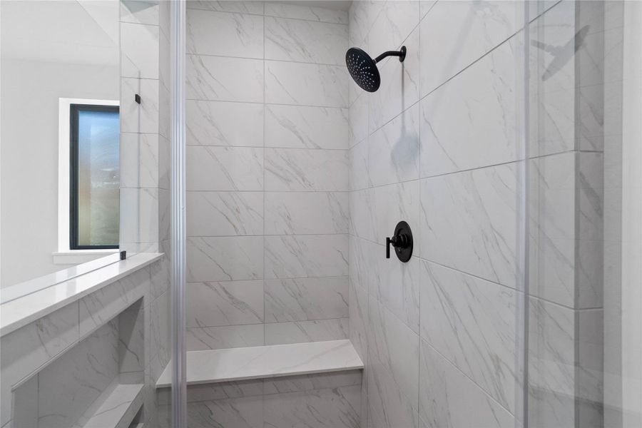 The walk-in shower includes a convenient, integrated bench with a niche shelf, offering comfort, extra storage space, and a high-end, custom appearance.