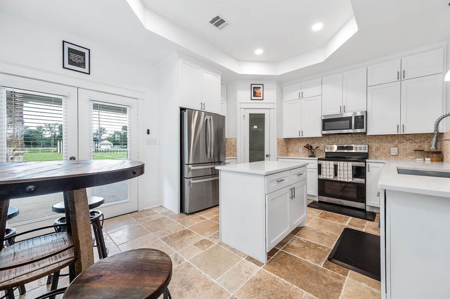 This modern kitchen offers a clean and functional layout with stainless steel appliances, abundant cabinetry, and a spacious center island perfect for meal prep and gathering. Large glass doors bring in natural light and provide easy access to the outdoor living space.