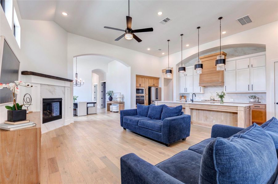 This spacious living area features an open floor plan with high ceilings, modern lighting, and large windows that allow natural light to flood in. It includes a cozy fireplace, stylish wood flooring, and a sleek kitchen with stainless steel appliances and a large island. The room is elegantly furnished with comfortable seating and tasteful decor. This spacious living area features an open floor plan with high ceilings, modern lighting, and large windows that allow natural light to flood in. It includes a cozy fireplace, stylish wood flooring, and a sleek kitchen with stainless steel appliances and a large island. The room is elegantly furnished with comfortable seating and tasteful decor.