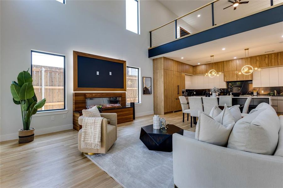 Living room with a towering ceiling, ceiling fan with notable chandelier, light wood-type flooring, and a wealth of natural light