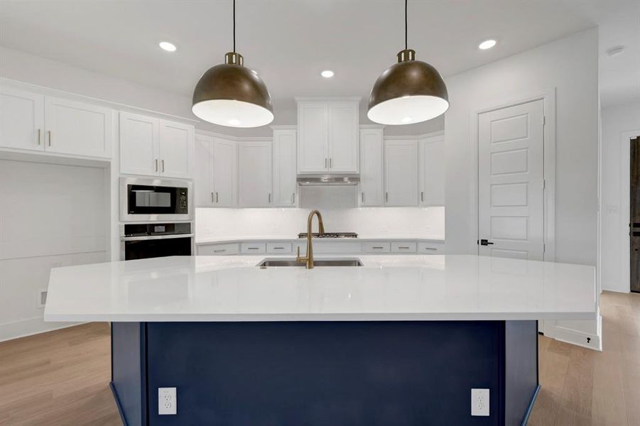 Two tone kitchen featuring two tone cabinets, oven, an island with sink, built in microwave, and light wood finished floors