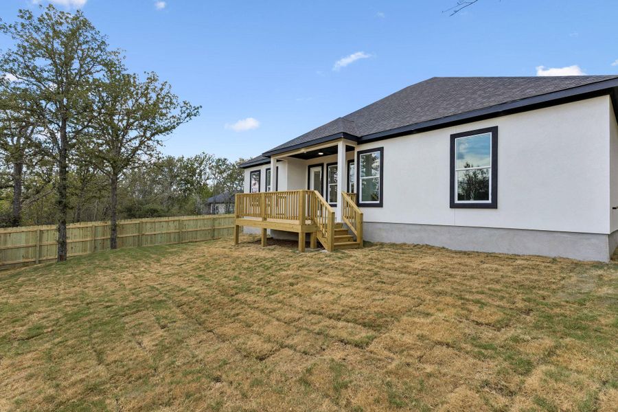 An elevated wooden deck overlooks a spacious, fully fenced yard lined with mature trees.