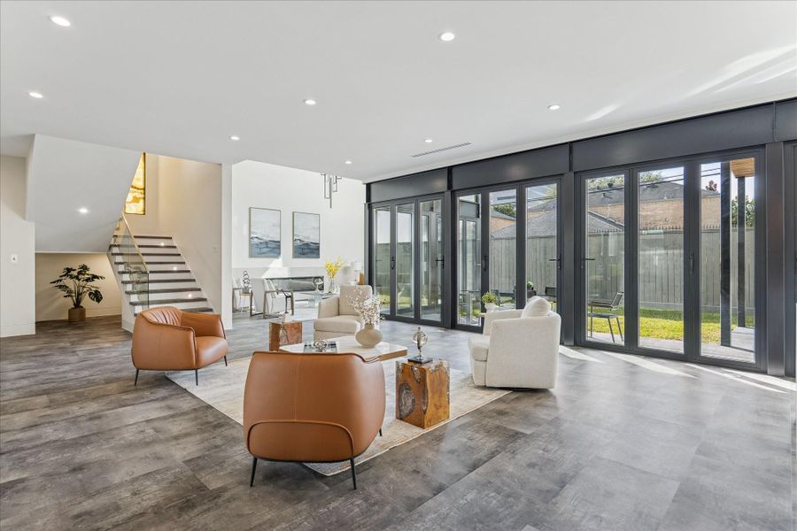 This spacious, modern living area features floor-to-ceiling glass doors offering abundant natural light and views of the backyard. Contemporary flooring, and an open staircase, providing a sleek, inviting atmosphere.