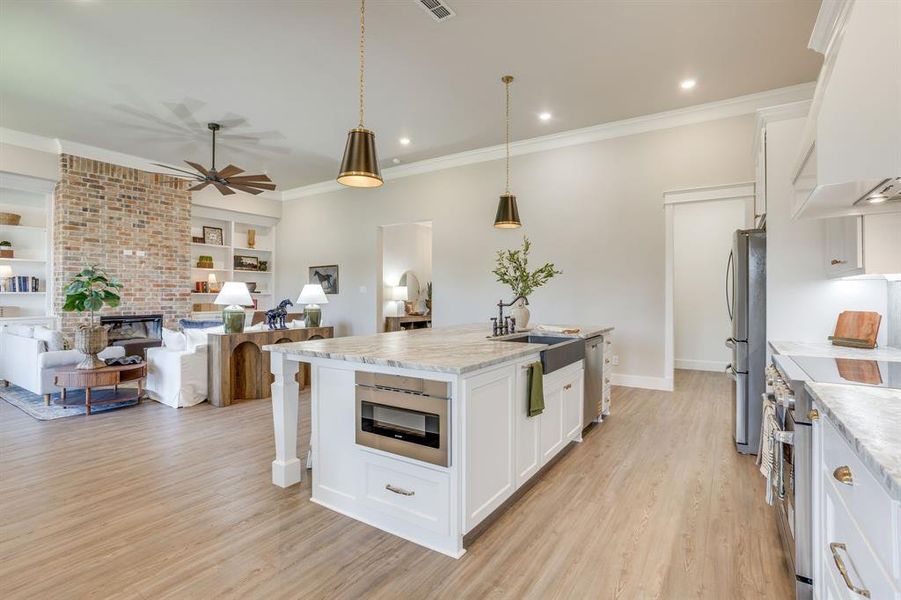 Open-concept living/kitchen space featuring wood-finish flooring, a kitchen island with stone countertop and farmhouse sink with stainless steel appliances