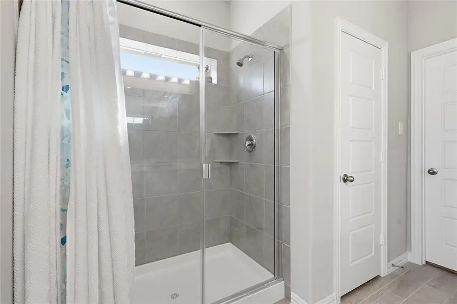 Shower enclosure featuring clear glass panels, a chrome showerhead, built-in tiled shelving, and a transom window