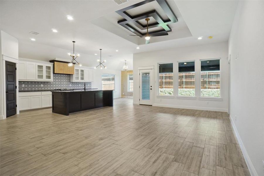 Kitchen with hanging light fixtures, ceiling fan with notable chandelier, coffered ceiling, backsplash, and a kitchen island with sink