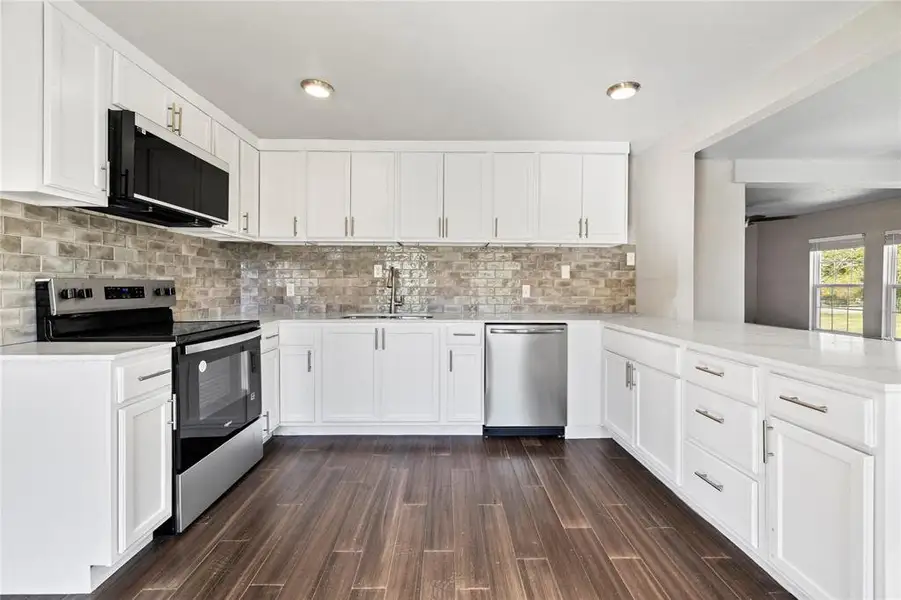 Kitchen featuring stainless steel appliances, white cabinets, decorative backsplash, light  countertops, and dark wood-style floors