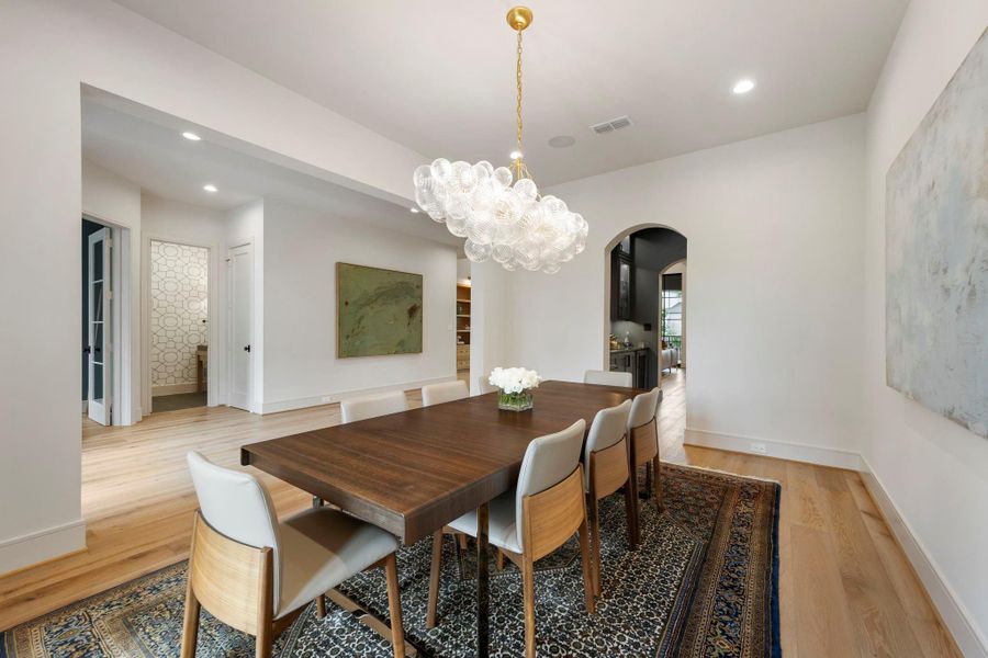 Refined dining space featuring a striking designer chandelier, warm wood floors, and a seamless connection to the butler’s pantry and wet bar for effortless entertaining.