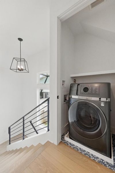 Laundry area with washer / dryer, wood finished floors, and a chandelier Laundry area with washer / dryer, wood finished floors, and a chandelier