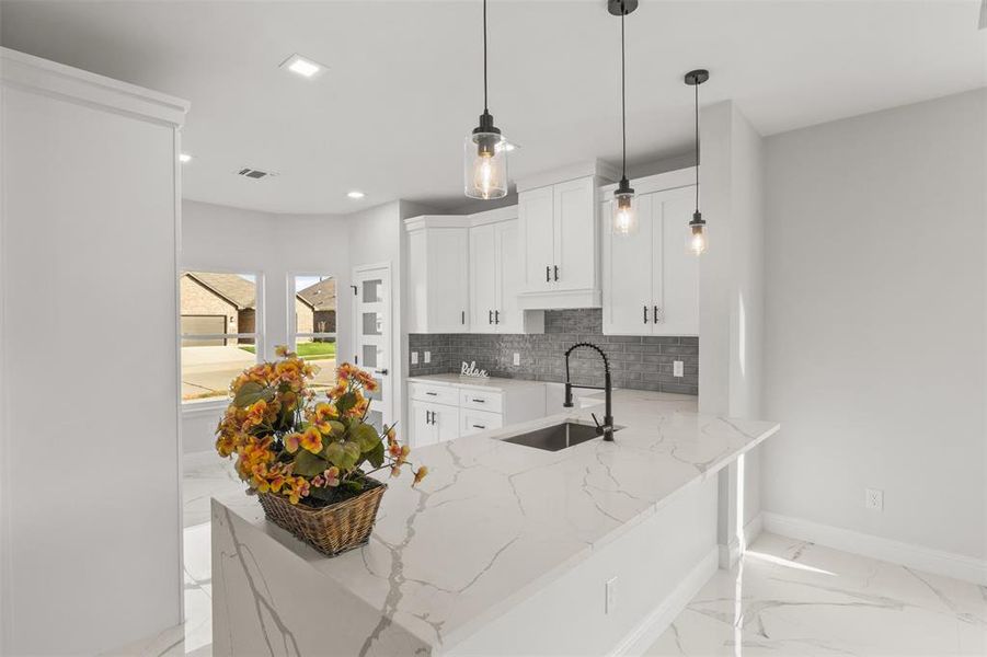 Kitchen featuring light stone counters, light marble finish floors, a peninsula, backsplash, and pendant lighting