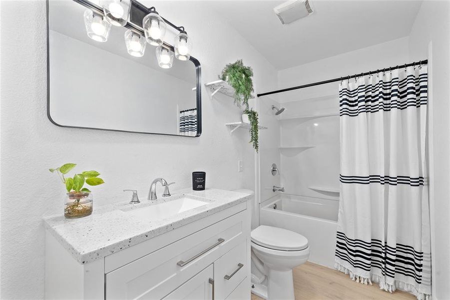 Bathroom with light wood-style floors, shower / bath combo with shower curtain, and vanity