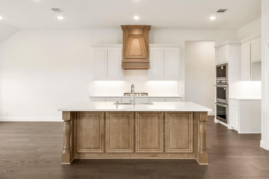 Kitchen with large wood island, white cabinets, wood range hood, and dark hardwood floors