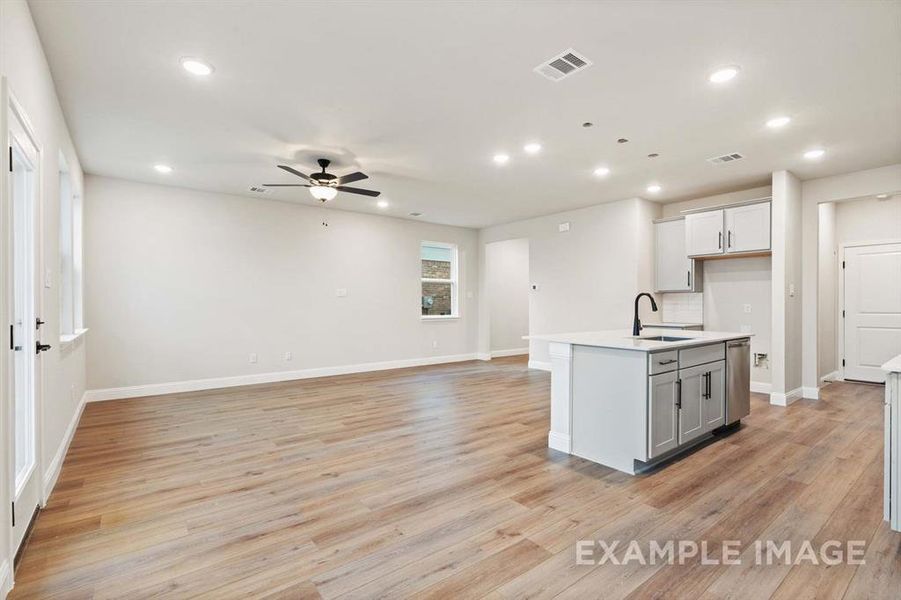 Kitchen featuring ceiling fan, sink, backsplash, an island with sink, and light wood-type flooring