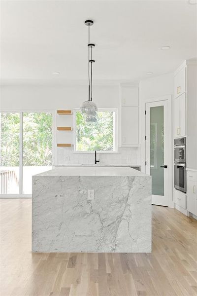 Kitchen with light hardwood / wood-style floors, white cabinets, decorative light fixtures, and stainless steel double oven