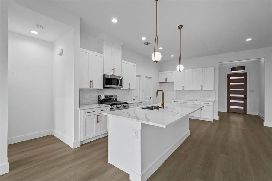 Kitchen featuring tasteful backsplash, stainless steel appliances, dark wood-style flooring, light stone counters, and an island with sink Kitchen featuring tasteful backsplash, stainless steel appliances, dark wood-style flooring, light stone counters, and an island with sink